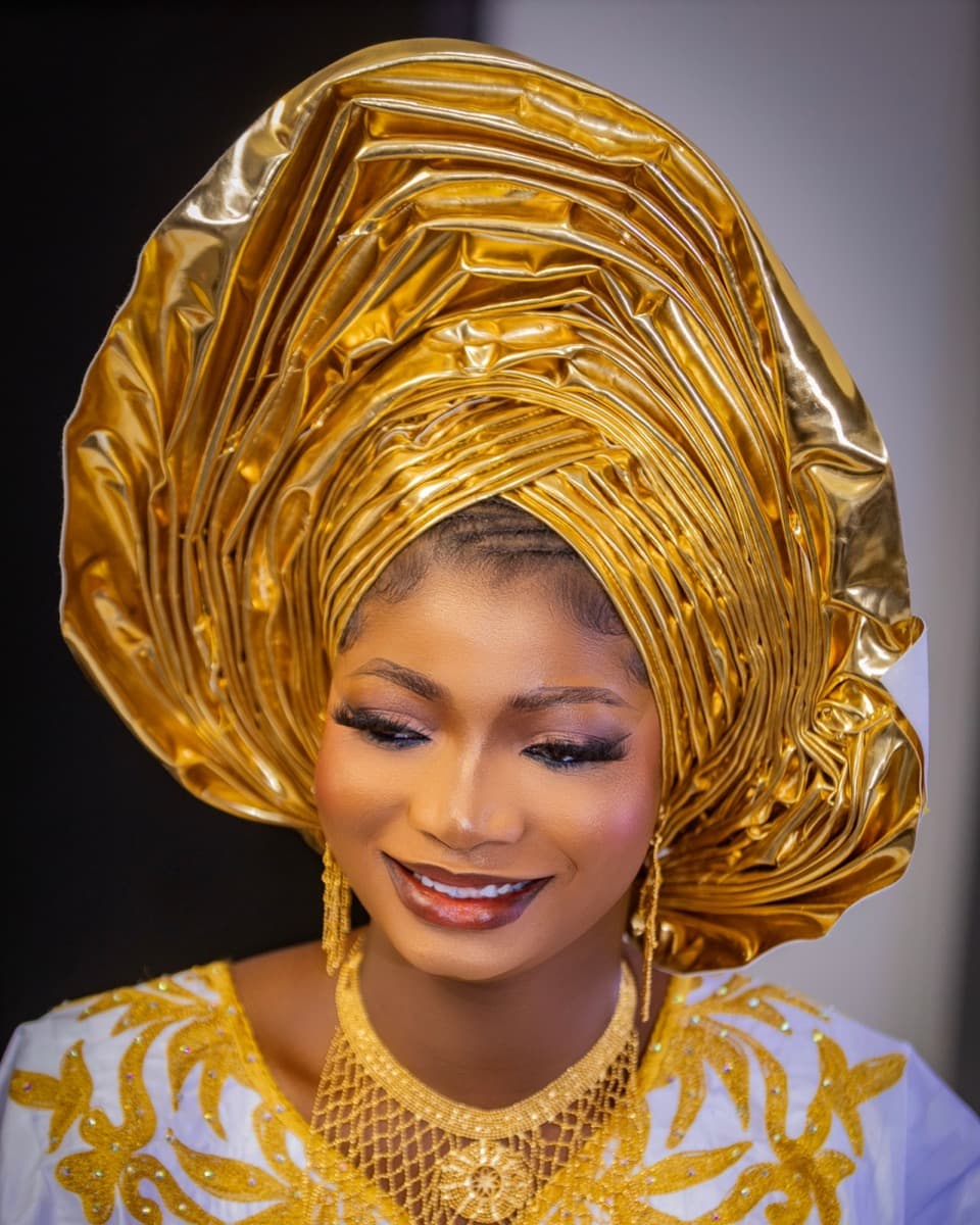 A woman wearing a tall, structured gold gele with clearly visible layered pleating