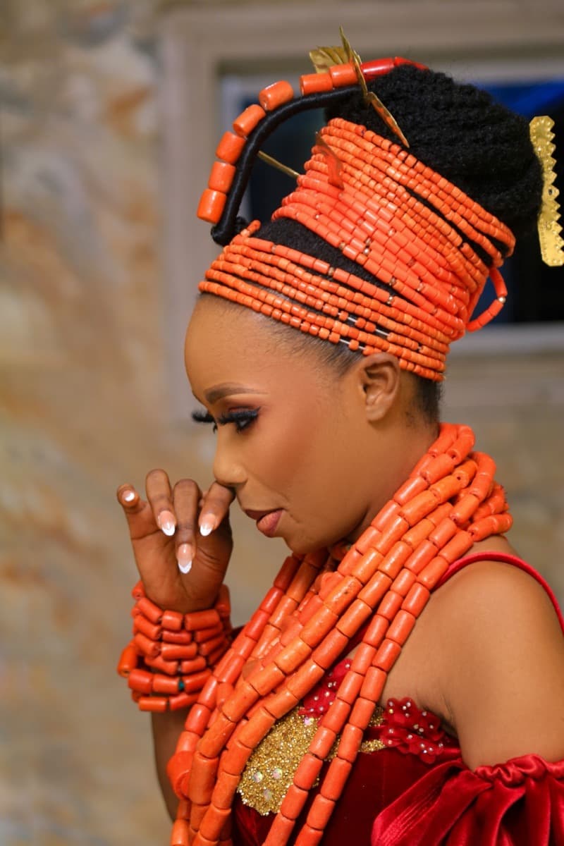 A woman in Niger Delta ceremonial dress wearing an elaborate coiled coral-bead headpiece and layered coral necklaces