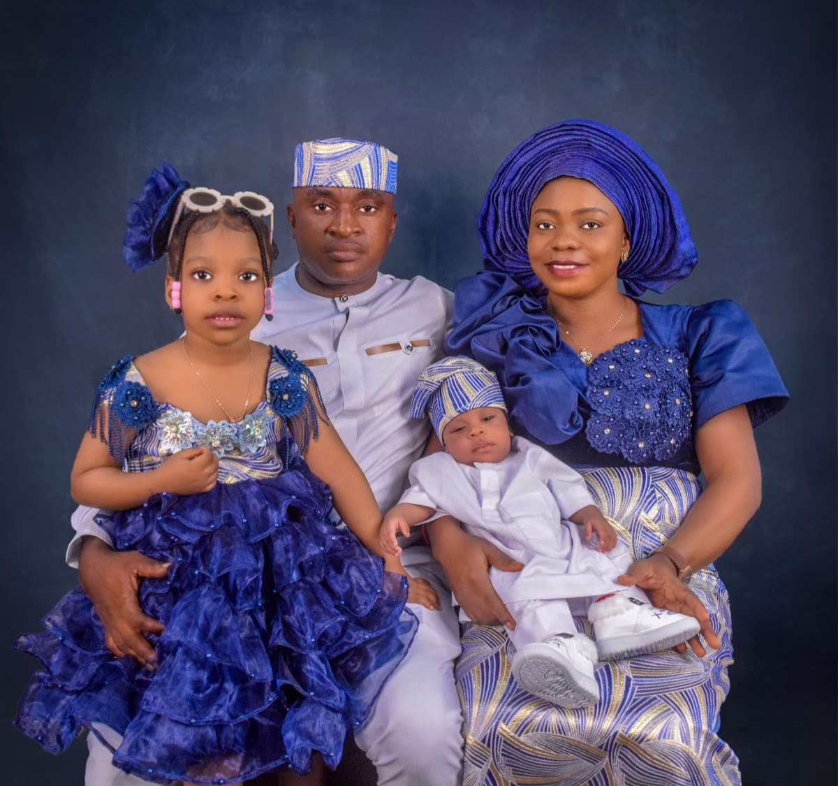 A family of four in matching royal-blue traditional outfits, including a young daughter and a baby, in a studio portrait