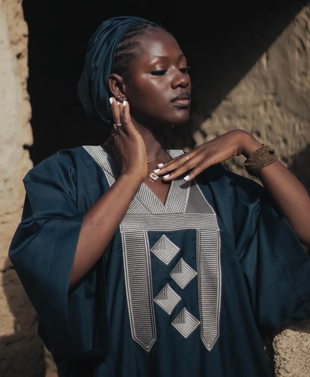 Close-up of a woman in a dark teal structured robe with a bold geometric embroidered chest panel of four stacked diamonds