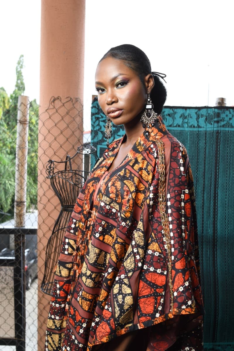 A woman in a bold orange, red, and brown printed oversized robe dress with dramatic wide sleeves, worn as a single full-length piece