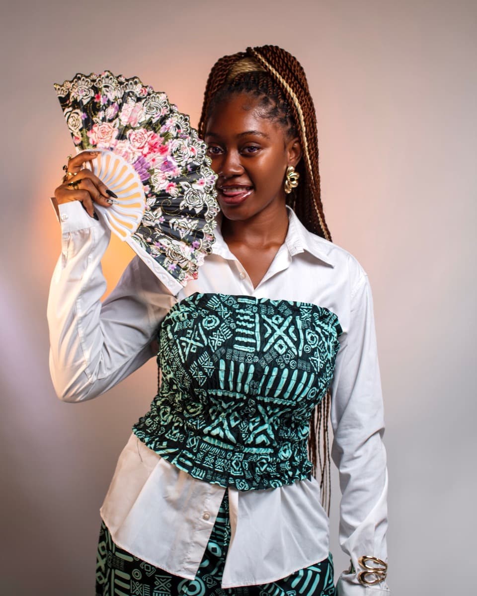 A woman in a structured black and teal geometric-print ankara corset bustier worn over a white shirt