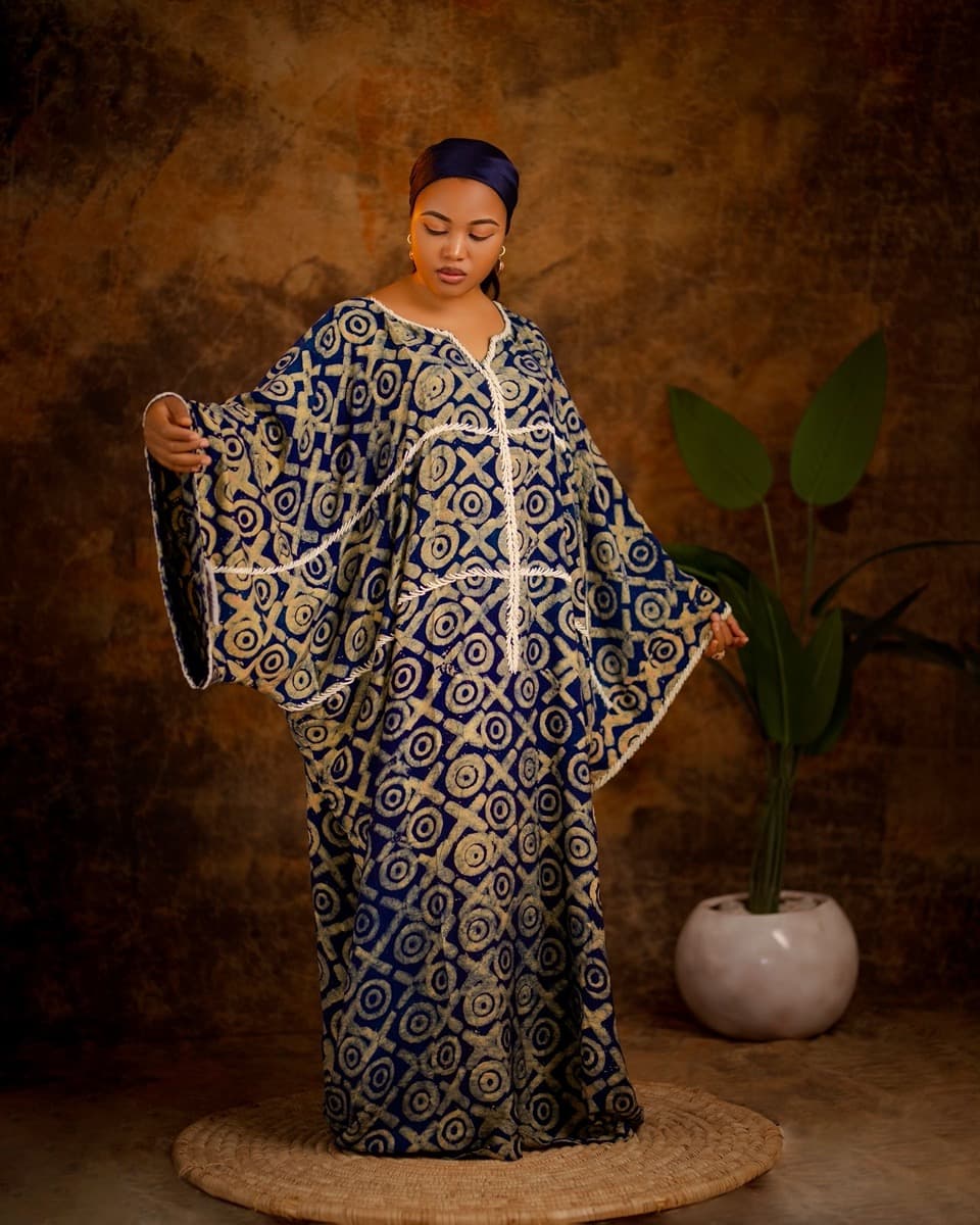 A woman in a navy and gold circular-motif bubu gown with dramatic wide batwing sleeves extended outward