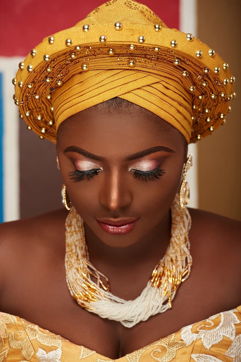 Close-up of a mustard-gold gele with visible gathered pleats and a full border of round gold beads stitched around the crown