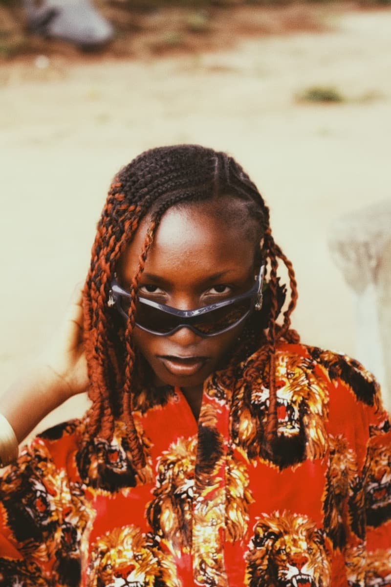 A young woman in a bold red isiagu lion-print shirt, styled with braided hair and sunglasses